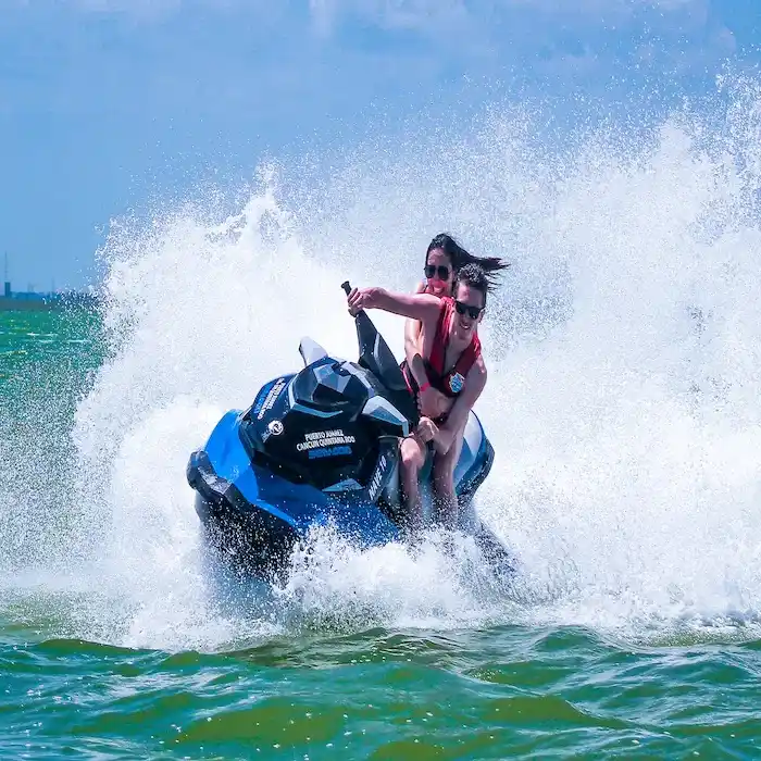 A young couple rides a jet ski at full speed, making a splash in the Cancun lagoon.