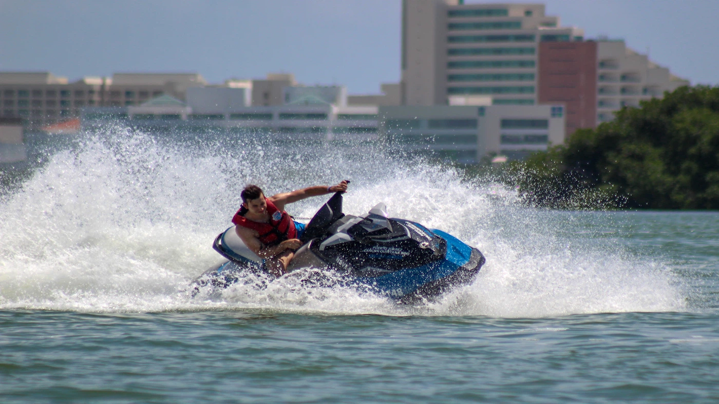 A young man riding a jet ski at full speed makes a splash at a jet ski rental in Cancun.